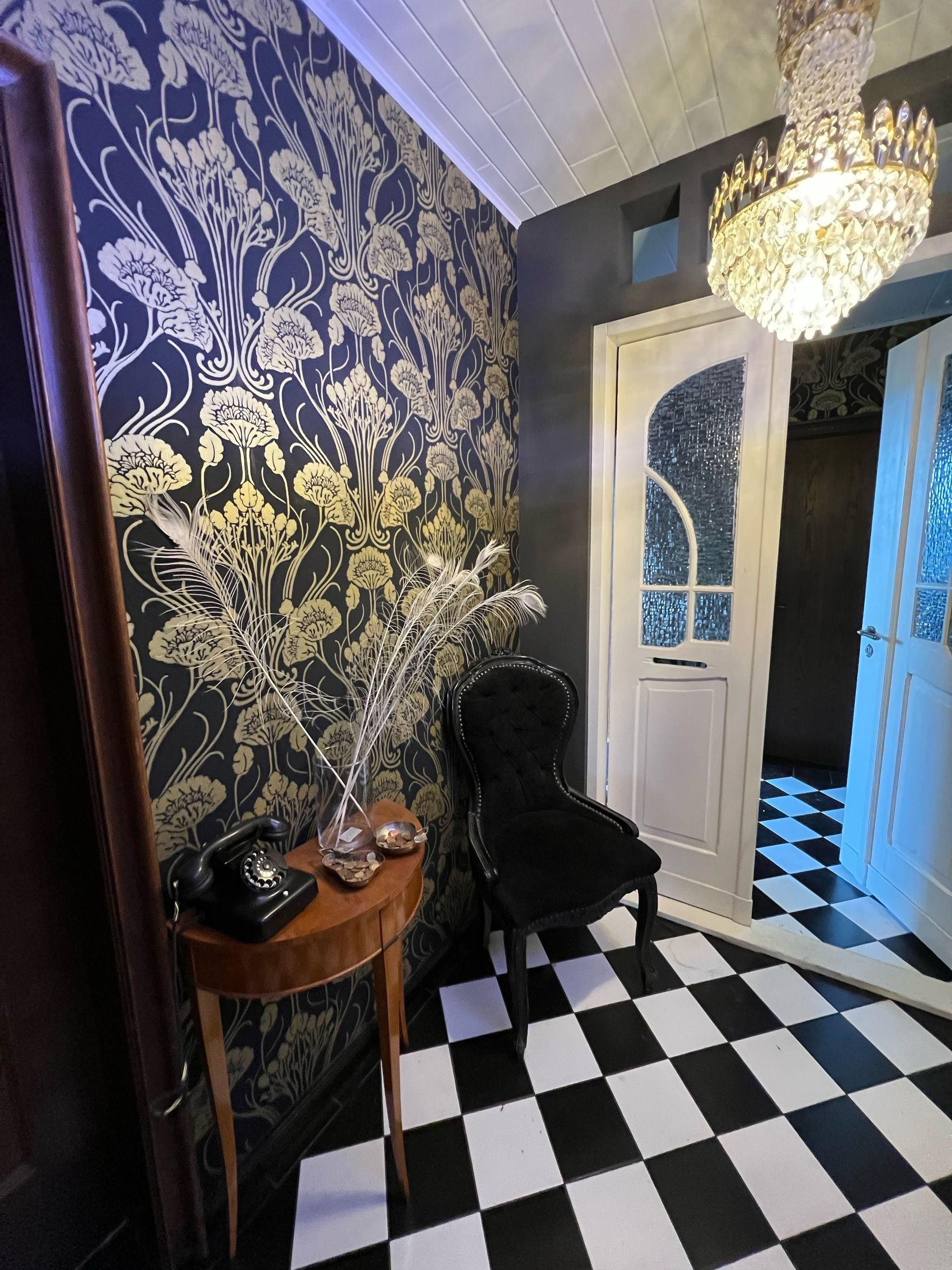 Ein Hausflur mit Türe, an der Wand eine schwarz Tapete mit goldenem Jugendstil Muster