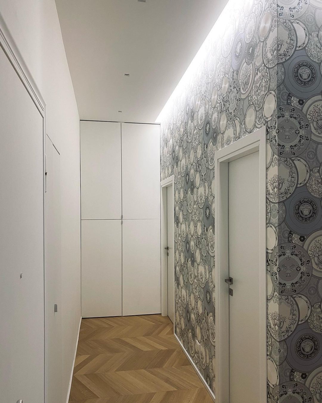 Ein Wohnungsflur mit zwei Türen, dessen Wand eine graue Tapete mit Versace-Tellermotiv ziert