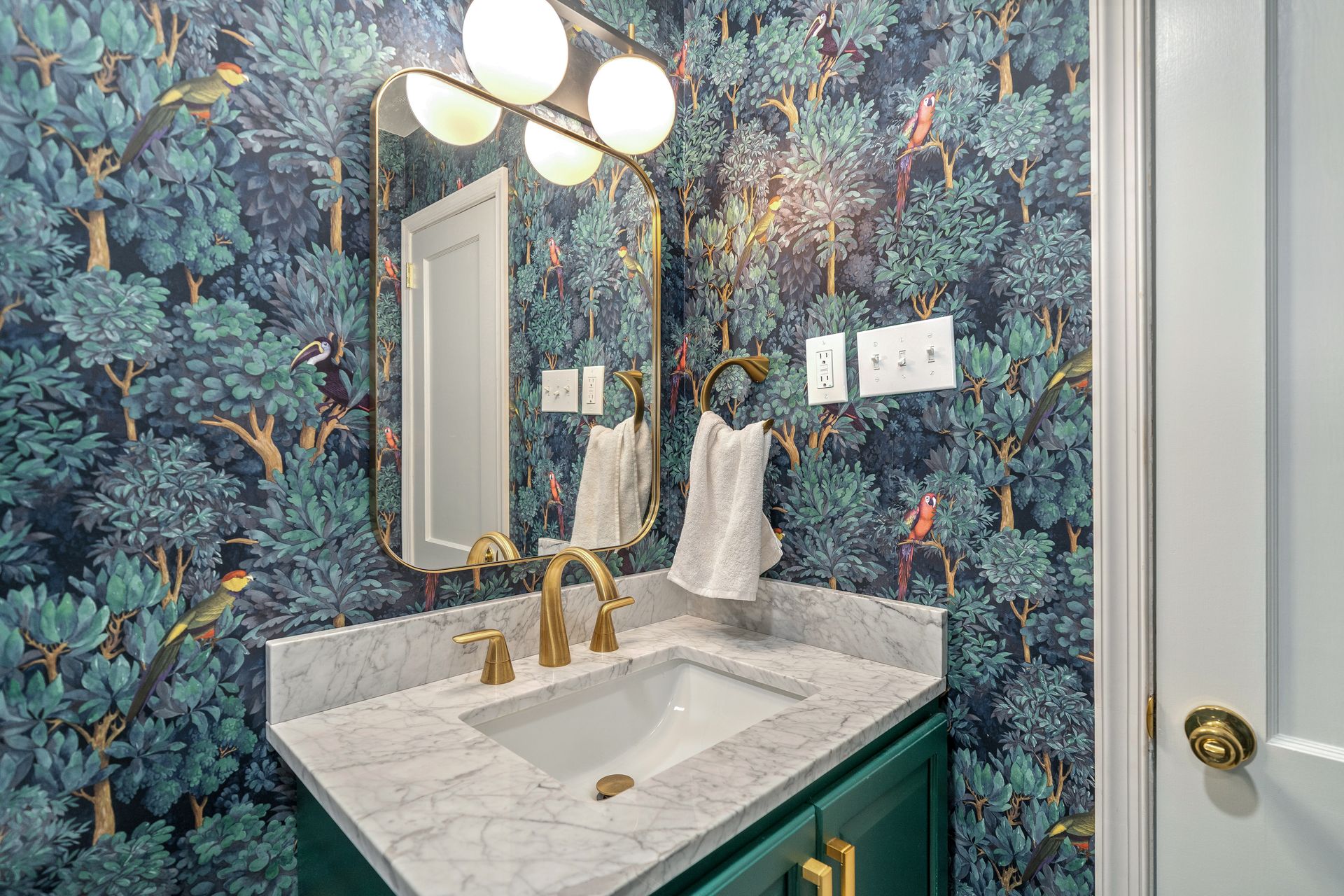 luxuriöses Badezimmer mit botanischer Tapete Amadori Green mit Vögeln und Bäumen, goldenen Armaturen, Marmorarbeitsplatte und türkisfarbenen Fliesen