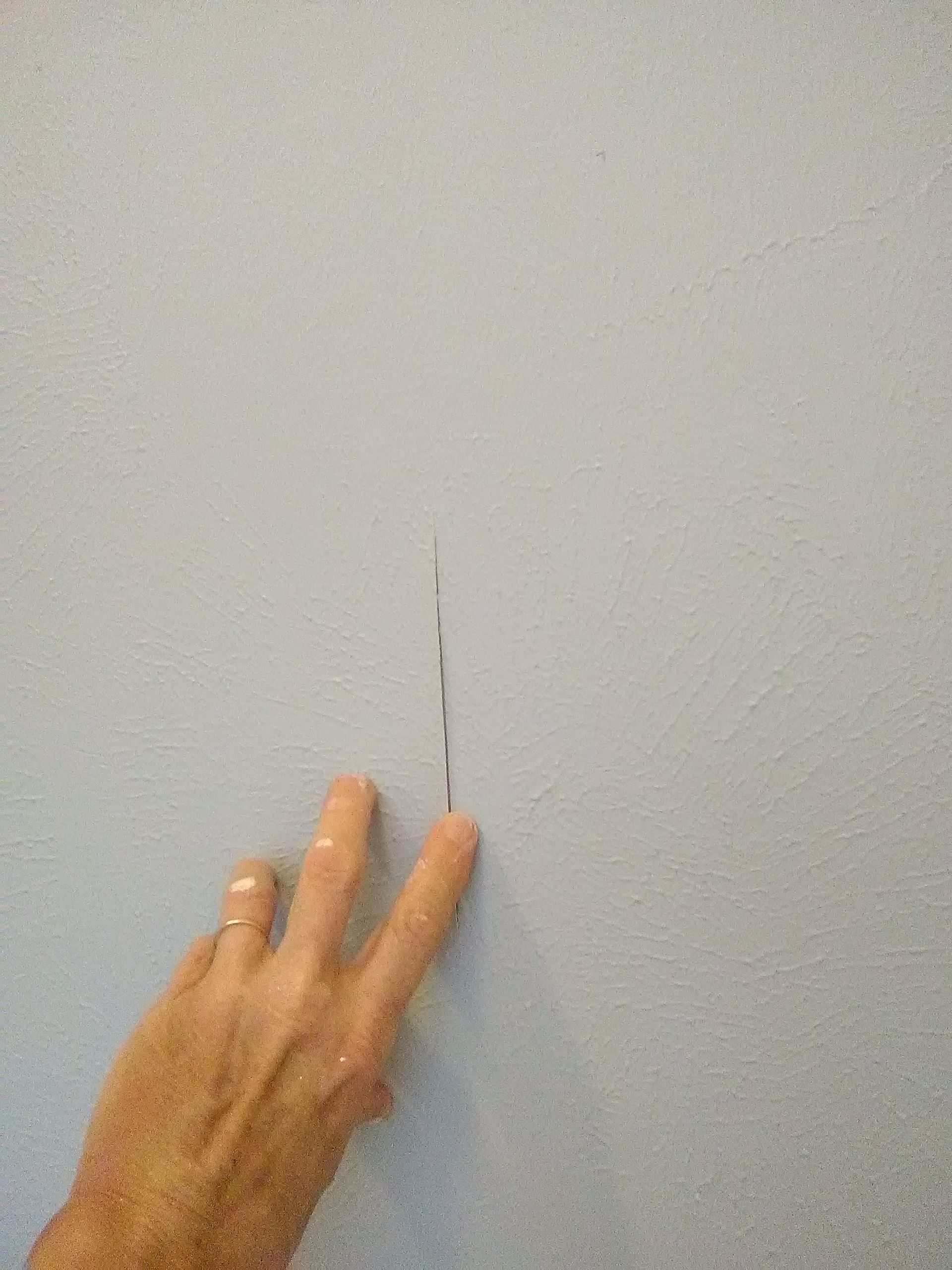 Nahaufnahme einer Hand, die auf einen dünnen Riss an einer bemalten Wandfläche zeigt