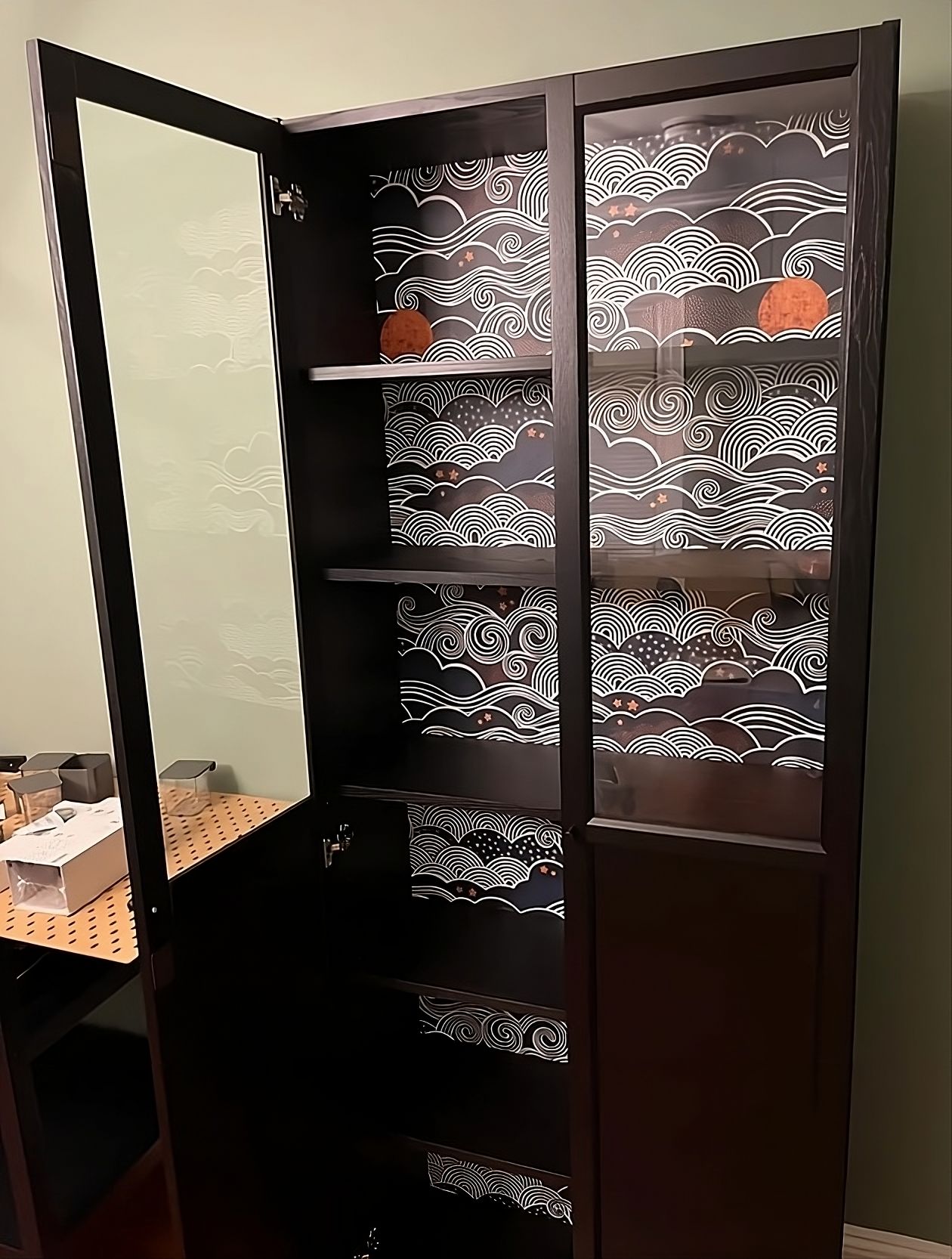 Ein mit Wellenmuster tapeziertes Glasvitrinen-Regal, ein kreatives DIY-IKEA-Hack für die Verschönerung von Möbeln.